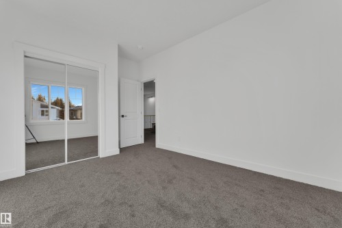 Bedroom featuring mirrored closet doors, neutral gray carpeting, white baseboards, and a white interior door with black hardware - 247 Linden Loop, Leduc, AB - Indoor Photo Showing Other Room
