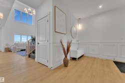 Bright entryway featuring light wood-finish flooring, white paneled walls, and a contemporary chandelier - 
