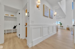 Spacious entryway featuring light wood-finish flooring, white wainscoting, and modern wall sconces - 