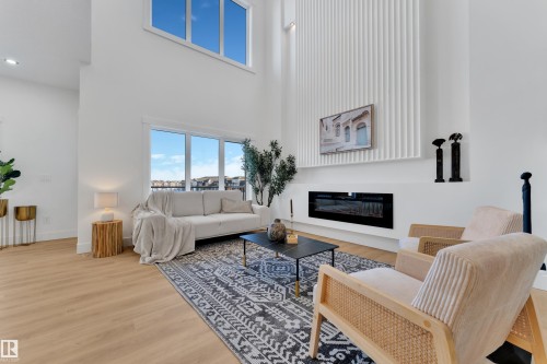 Vaulted ceiling great room featuring a linear electric fireplace, full-height decorative paneling, wood-finish flooring, and large windows - 247 Linden Loop, Leduc, AB - Indoor Photo Showing Living Room With Fireplace