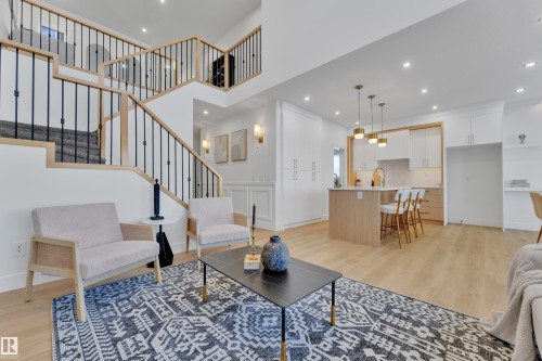 Open-concept living space featuring wood-finish flooring, a contemporary kitchen with an island, and a prominent staircase with black metal balusters and light wood railings - 247 Linden Loop, Leduc, AB - Indoor Photo Showing Living Room