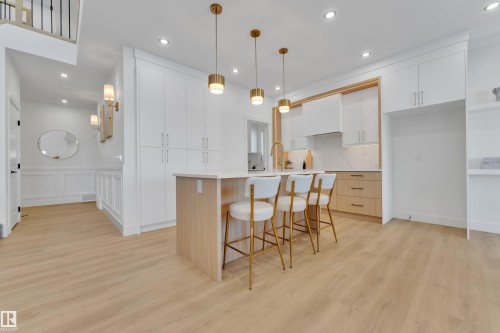 Open-concept kitchen featuring an island with seating, white shaker cabinetry, light wood-finish lower cabinetry, a light-toned backsplash, and wood-finish flooring - 247 Linden Loop, Leduc, AB - Indoor Photo Showing Kitchen With Upgraded Kitchen
