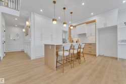 Open-concept kitchen featuring an island with seating, white shaker cabinetry, light wood-finish lower cabinetry, a light-toned backsplash, and wood-finish flooring - 
