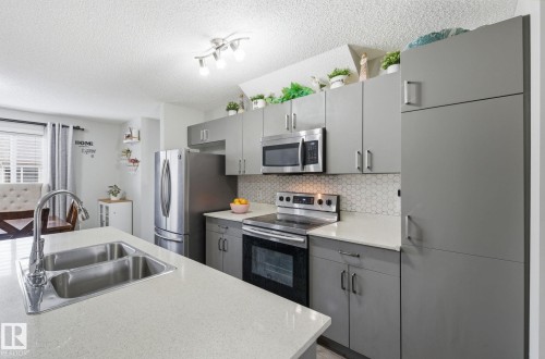 Modern kitchen featuring sleek gray cabinetry, stainless steel appliances, a double basin sink, and white countertops - 4636 175 Ave, Edmonton, AB - Indoor Photo Showing Kitchen With Double Sink