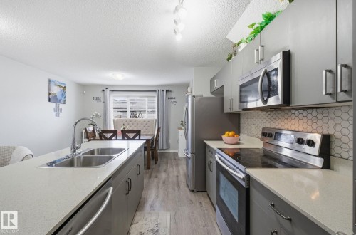 The kitchen features stainless steel appliances, grey cabinetry, light-colored countertops, and a white hexagonal tile backsplash - 4636 175 Ave, Edmonton, AB - Indoor Photo Showing Kitchen With Double Sink