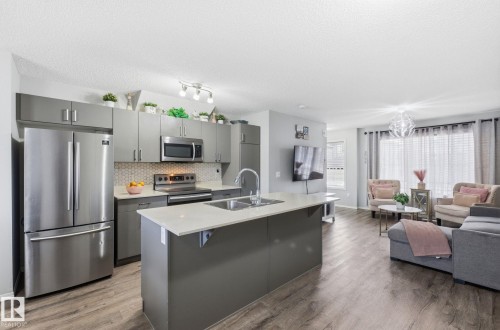 The open concept living area features resilient plank flooring and a kitchen with stainless steel appliances, a white quartz countertop island, and gray cabinetry - 4636 175 Ave, Edmonton, AB - Indoor Photo Showing Kitchen With Double Sink