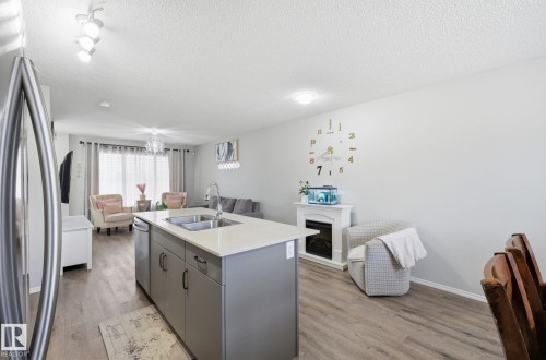 This open-concept area features a kitchen island with a double sink and light-colored countertop, alongside wood-look flooring throughout - 4636 175 Ave, Edmonton, AB - Indoor Photo Showing Kitchen With Double Sink