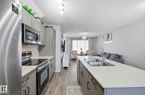 The kitchen features stainless steel appliances, grey cabinetry, a tiled backsplash, and a kitchen island with a double sink and ample countertop space - 4636 175 Ave, Edmonton, AB - Indoor Photo Showing Kitchen With Double Sink With Upgraded Kitchen