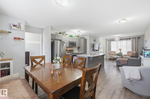 This open-concept living space features hardwood flooring, a spacious dining area, and a kitchen with stainless steel appliances and a center island - 4636 175 Ave, Edmonton, AB - Indoor