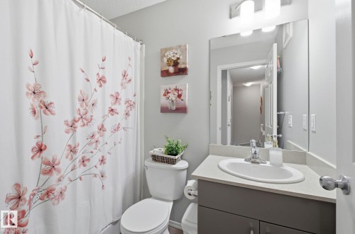 The bathroom features a toilet, a vanity with a sink and a mirror, and a shower with a shower curtain - 4636 175 Ave, Edmonton, AB - Indoor Photo Showing Bathroom