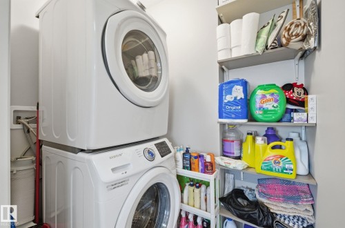 This utility space features a modern stacked washer and dryer, accompanied by wall-mounted shelving for organized storage - 4636 175 Ave, Edmonton, AB - Indoor Photo Showing Laundry Room