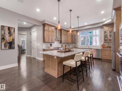 Gourmet kitchen featuring a large island with seating, stainless steel appliances, light wood cabinetry, and recessed lighting - 