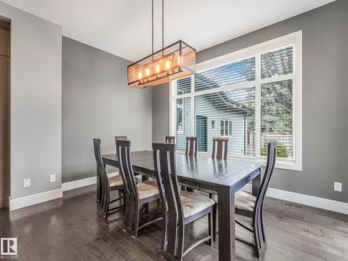 Dining area featuring a large window, dark wood-finish flooring, a contemporary linear chandelier, and a neutral wall color with white trim - 8927 120 Street, Edmonton, AB - Indoor Photo Showing Dining Room
