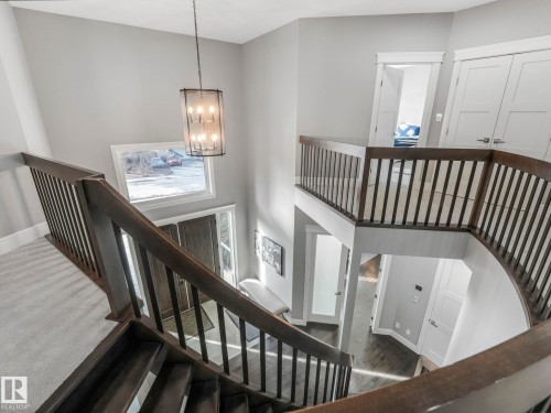 Multi-level interior featuring a contemporary chandelier, hardwood staircase with dark wood banister, and light grey wall finishes - 8927 120 Street, Edmonton, AB - Indoor Photo Showing Other Room
