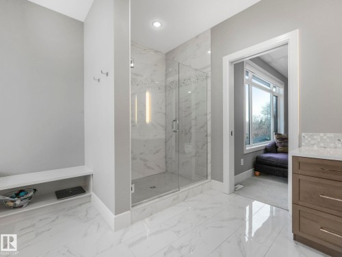Spacious bathroom featuring a glass-enclosed shower with full-height tile surround, marble-look floor tiling, and a built-in wood-finish vanity with a light-toned countertop - 8927 120 Street, Edmonton, AB - Indoor Photo Showing Bathroom