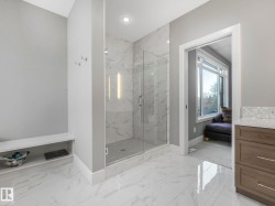 Spacious bathroom featuring a glass-enclosed shower with full-height tile surround, marble-look floor tiling, and a built-in wood-finish vanity with a light-toned countertop - 