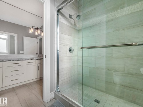 Glass-enclosed shower with tiled walls and a separate vanity area featuring white cabinetry, a light-toned countertop, and modern lighting fixtures - 8927 120 Street, Edmonton, AB - Indoor Photo Showing Bathroom