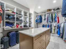 Walk-in closet featuring an expansive central island with a light-toned countertop and integrated drawers, extensive built-in shelving, multiple hanging rods, recessed lighting, and large format floor tiling - 