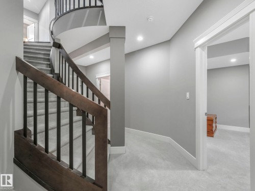 Curved staircase featuring dark wood newel posts and handrails with black metal balusters - 8927 120 Street, Edmonton, AB - Indoor Photo Showing Other Room