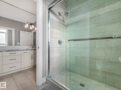 Glass-enclosed shower with tiled walls and a separate vanity area featuring white cabinetry, a light-toned countertop, and modern lighting fixtures - 