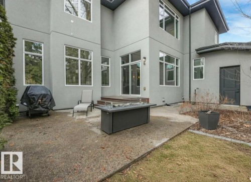 Rear exterior featuring a large concrete patio, an elevated wood deck, and multiple oversized windows with white frames - 8927 120 Street, Edmonton, AB - Outdoor With Exterior