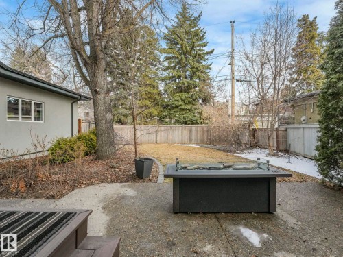 Expansive concrete patio with a built-in fire pit, surrounded by a fenced yard and mature landscaping - 8927 120 Street, Edmonton, AB - Outdoor