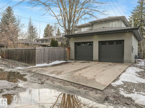Contemporary stucco exterior featuring a two-car garage with dark gray doors, upper-level windows, and a private wooden fence - 8927 120 Street, Edmonton, AB - Outdoor