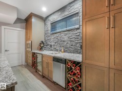 Wet bar featuring a textured stone accent wall, granite countertops, wood-finish cabinetry, built-in wine storage, and stainless steel appliances - 