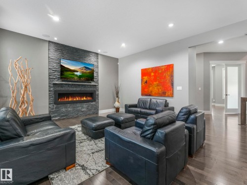 Living room with a stacked stone accent wall, linear electric fireplace, recessed lighting, and wood-finish flooring - 8927 120 Street, Edmonton, AB - Indoor Photo Showing Living Room With Fireplace