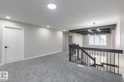 Upper-level landing featuring textured gray carpeting, recessed ceiling lighting, and a modern black chandelier - 