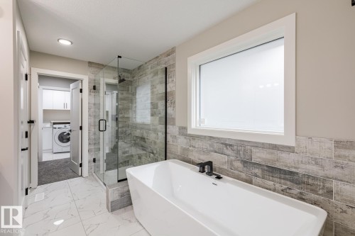 Freestanding soaking tub with matte black fixtures, set against a tiled accent wall - 48 Chartres Close, St. Albert, AB - Indoor Photo Showing Bathroom