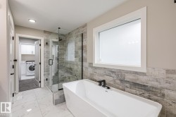 Freestanding soaking tub with matte black fixtures, set against a tiled accent wall - 