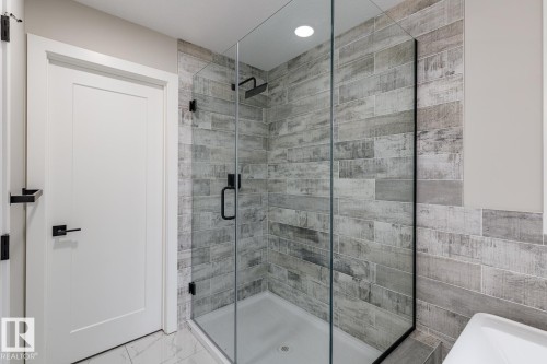 Walk-in shower featuring a glass enclosure, wood-finish tile surround, and matte black fixtures - 48 Chartres Close, St. Albert, AB - Indoor Photo Showing Bathroom