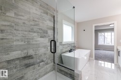 Modern bathroom featuring a frameless glass shower enclosure and a freestanding soaking tub with a wall-mounted faucet - 