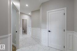 Hallway featuring marble-look tile flooring, white wainscoting, flush-panel doors with black hardware, and recessed lighting - 