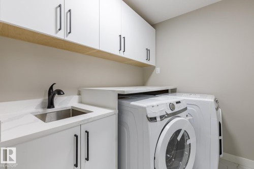 Laundry area featuring white cabinetry with matte black hardware, a stainless steel sink, a black faucet, and white countertops - 48 Chartres Close, St. Albert, AB - Indoor Photo Showing Laundry Room