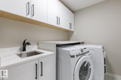 Laundry area featuring white cabinetry with matte black hardware, a stainless steel sink, a black faucet, and white countertops - 
