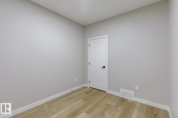 Neutral-toned room featuring light wood-finish flooring, white baseboards, and a contemporary white door with matte black hardware - 