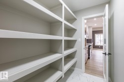Walk-in pantry featuring extensive built-in shelving, white marble-look flooring, and a frosted glass panel door - 