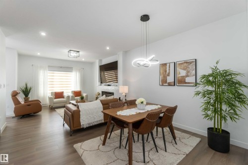 Open-concept living and dining areas featuring wood-finish flooring, recessed lighting, and a modern linear chandelier - 124 28 Street, Edmonton, AB 