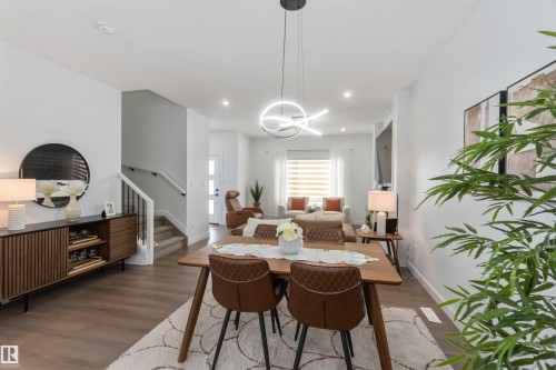 Open concept dining area featuring wood-finish flooring, a contemporary chandelier, a built-in staircase with metal balusters, and recessed ceiling lighting - 124 28 Street, Edmonton, AB 
