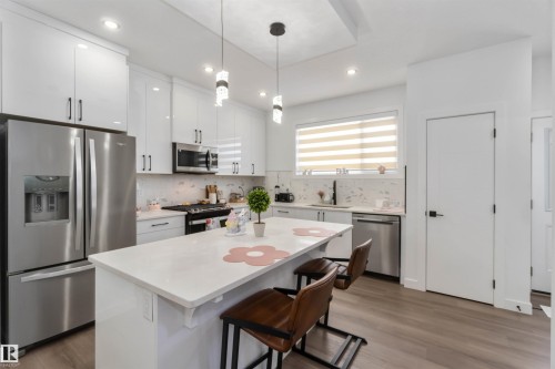 Modern kitchen featuring white cabinetry, stainless steel appliances, a center island with countertop seating, and wood-finish flooring - 124 28 Street, Edmonton, AB 