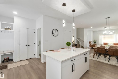Open-concept living space featuring wood-finish flooring, a white kitchen island with dark hardware, recessed lighting, and modern pendant fixtures - 124 28 Street, Edmonton, AB 