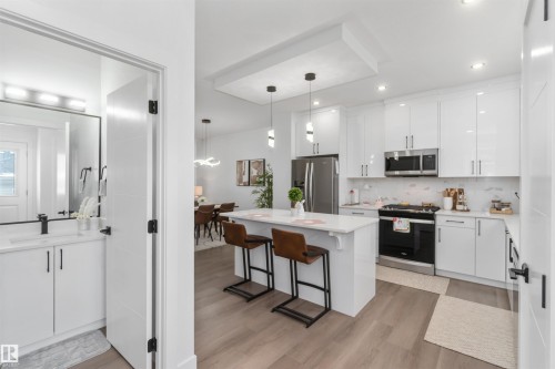 Open-concept kitchen featuring white cabinetry, stainless steel appliances, a center island with pendant lighting, and wood-finish flooring - 124 28 Street, Edmonton, AB 