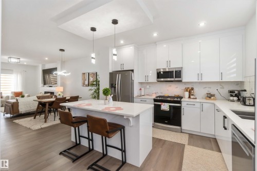 Modern kitchen featuring white shaker-style cabinetry, stainless steel appliances, and a central island with counter seating - 124 28 Street, Edmonton, AB 