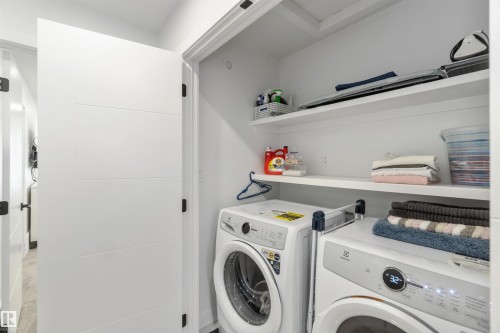 Dedicated laundry closet featuring a stacked washer and dryer, integrated shelving, and white walls - 124 28 Street, Edmonton, AB 