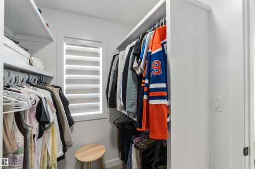 Walk-in closet featuring white built-in shelving, hanging rods, an integrated window, and neutral wall finishes - 124 28 Street, Edmonton, AB 