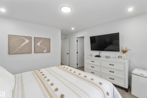 Recessed lighting illuminates a space featuring a white door with black hardware, a wall-mounted flat-screen television, and light-colored carpeting - 124 28 Street, Edmonton, AB 