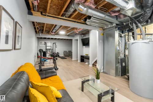 Finished basement area featuring wood-finish flooring, light grey walls, and exposed ceiling joists with visible ductwork - 124 28 Street, Edmonton, AB 