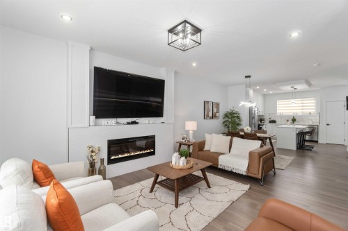 Open-concept living area featuring wood-finish flooring, recessed lighting, and a linear electric fireplace - 124 28 Street, Edmonton, AB 